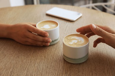 Photo of Friends drinking coffee at wooden table in cafe, closeup