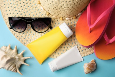 Beach accessories and sunscreen on light blue background, flat lay