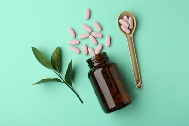 Photo of Vitamin pills, bottle, spoon and branch on mint color background, flat lay