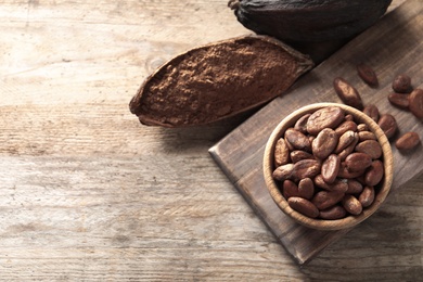 Flat lay composition with cocoa beans and powder on wooden table, space for text