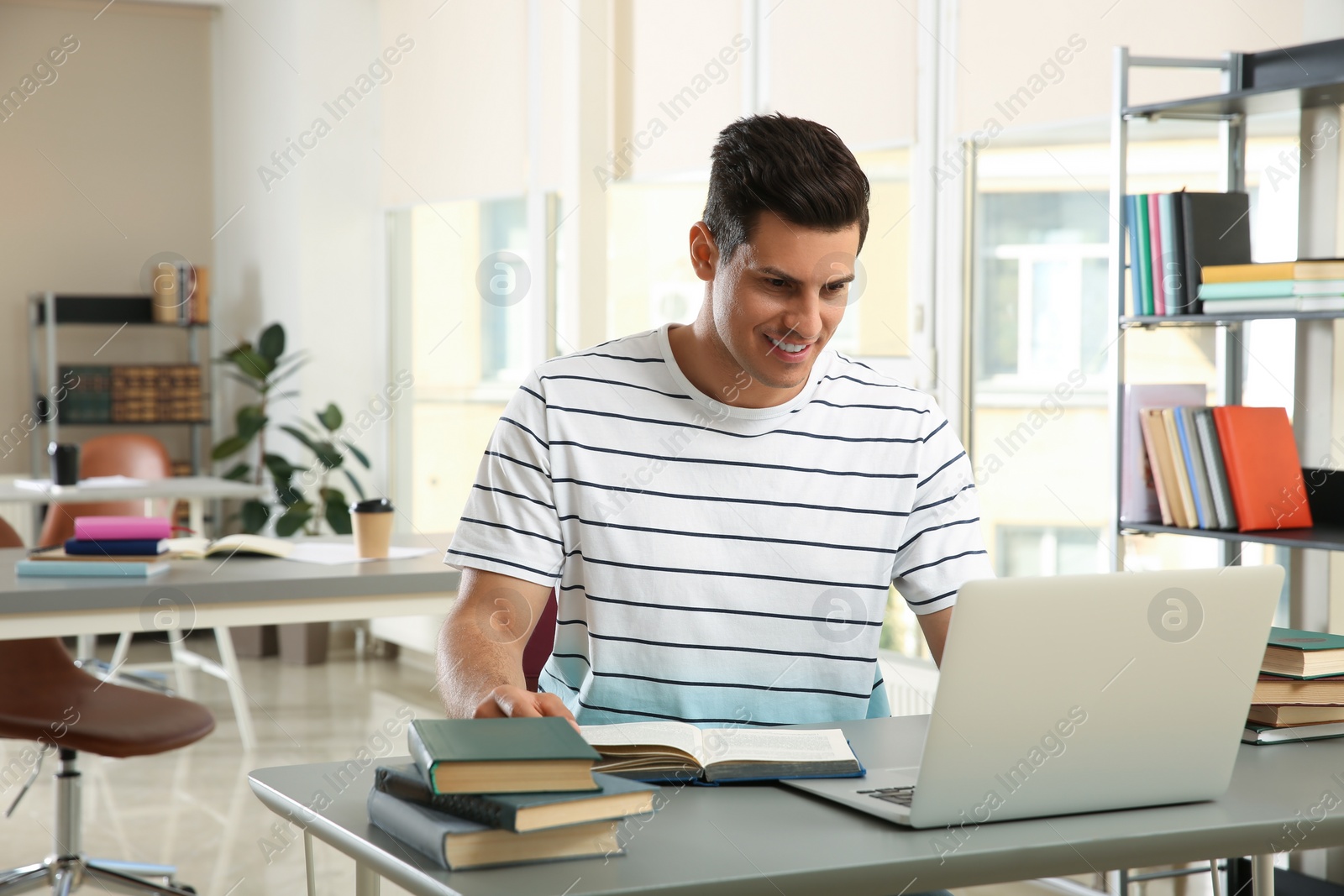 Photo of Man with laptop studying at table in library