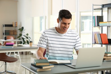 Photo of Man with laptop studying at table in library