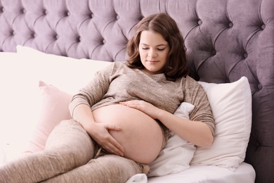 Photo of Young pregnant woman lying on bed at home