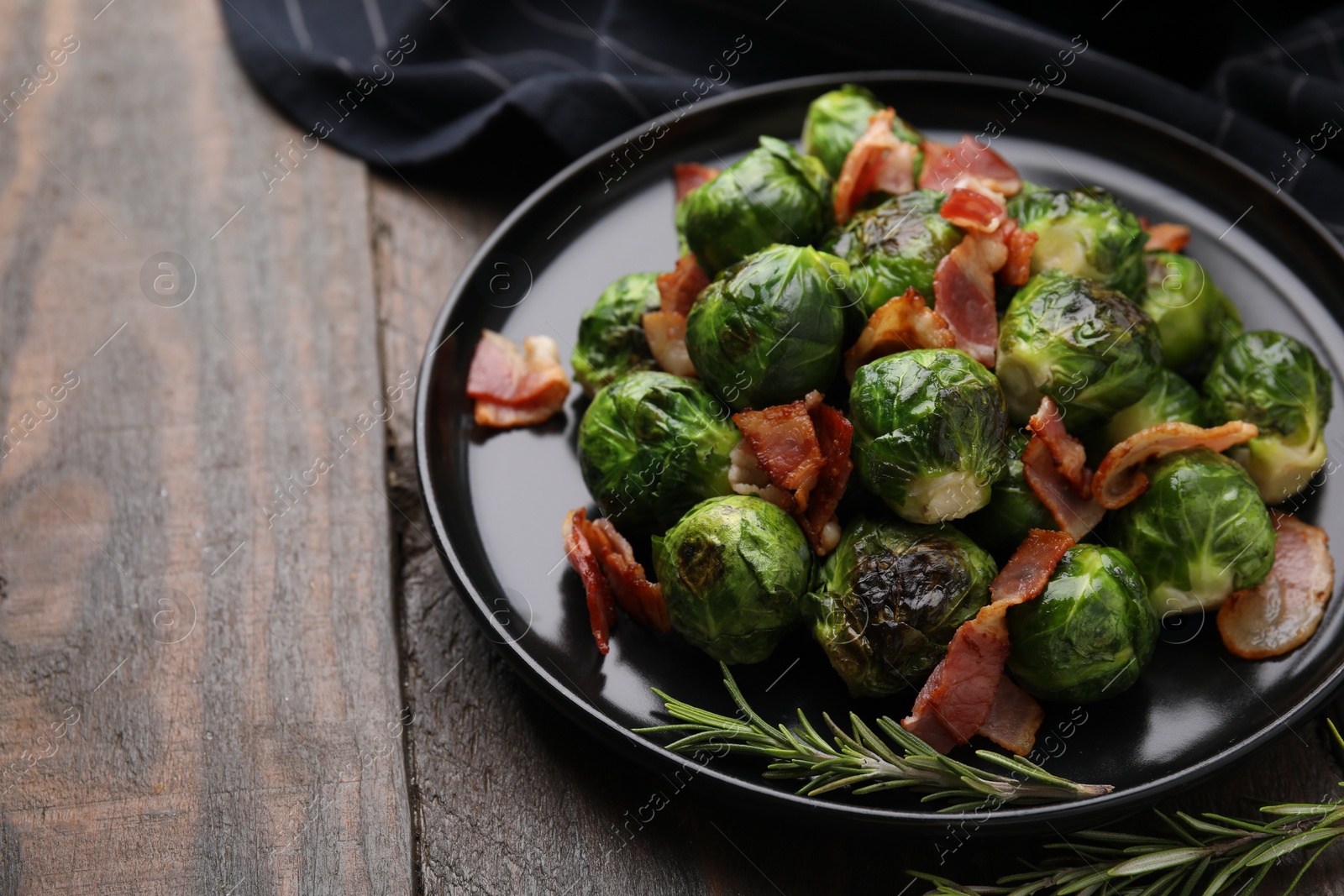 Photo of Delicious roasted Brussels sprouts, bacon and rosemary on wooden table, closeup. Space for text