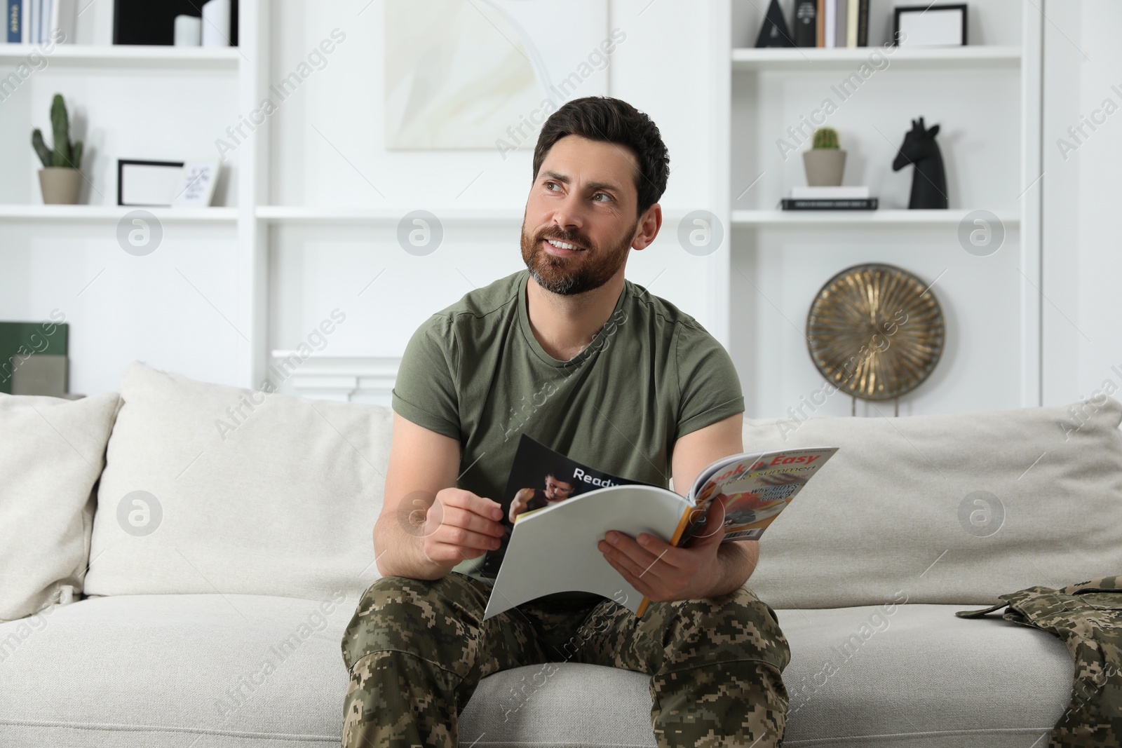 Photo of Soldier with magazine on sofa in living room. Military service