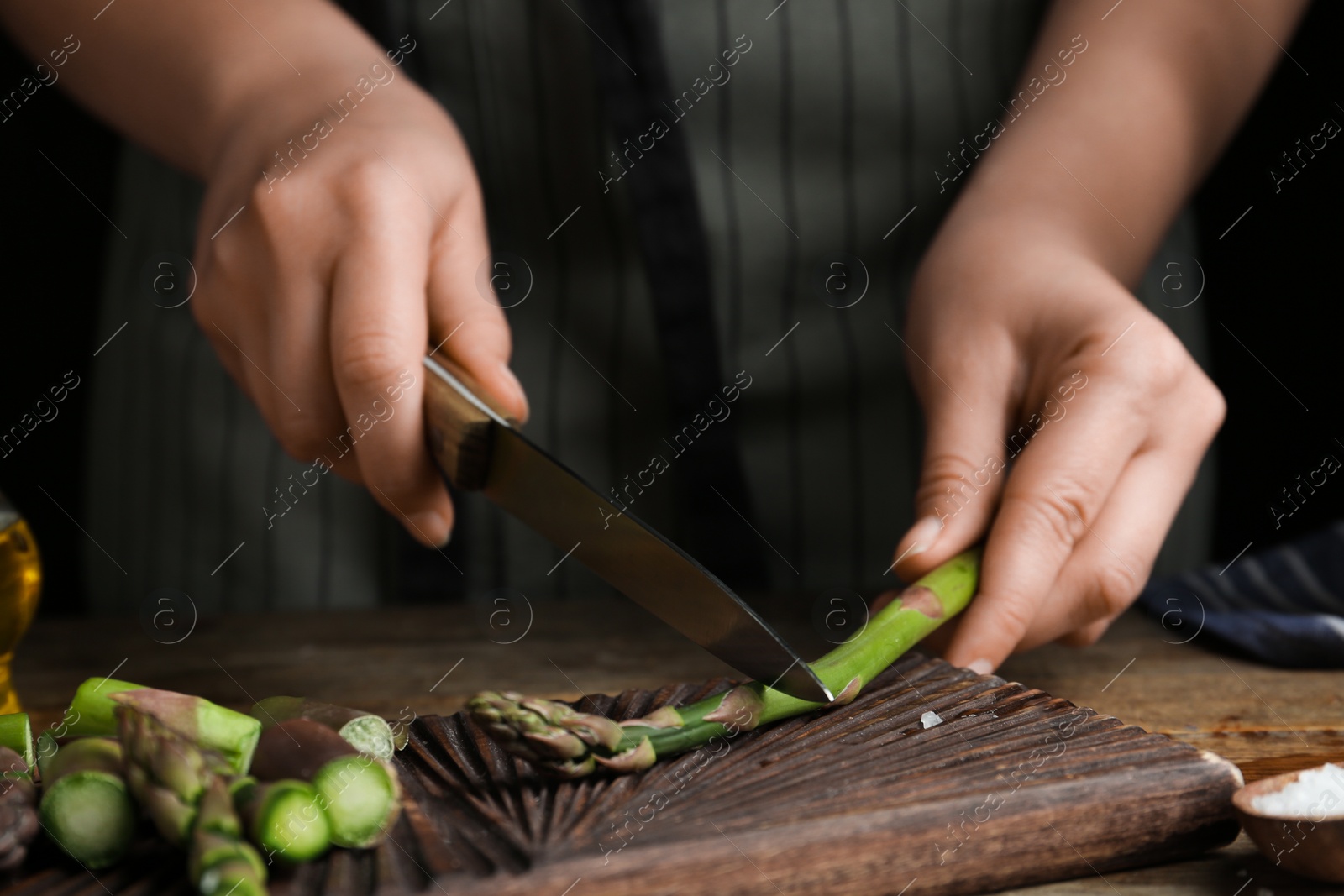 Photo of Woman cutting asparagus at wooden table, closeup