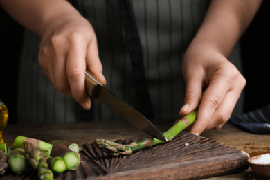 Woman cutting asparagus at wooden table, closeup