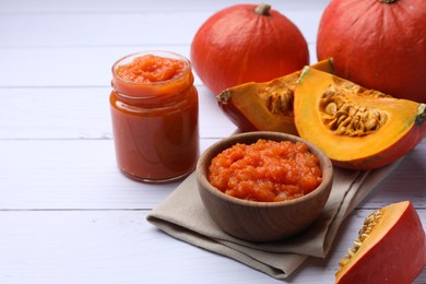 Delicious pumpkin jam and fresh pumpkins on white wooden table, space for text