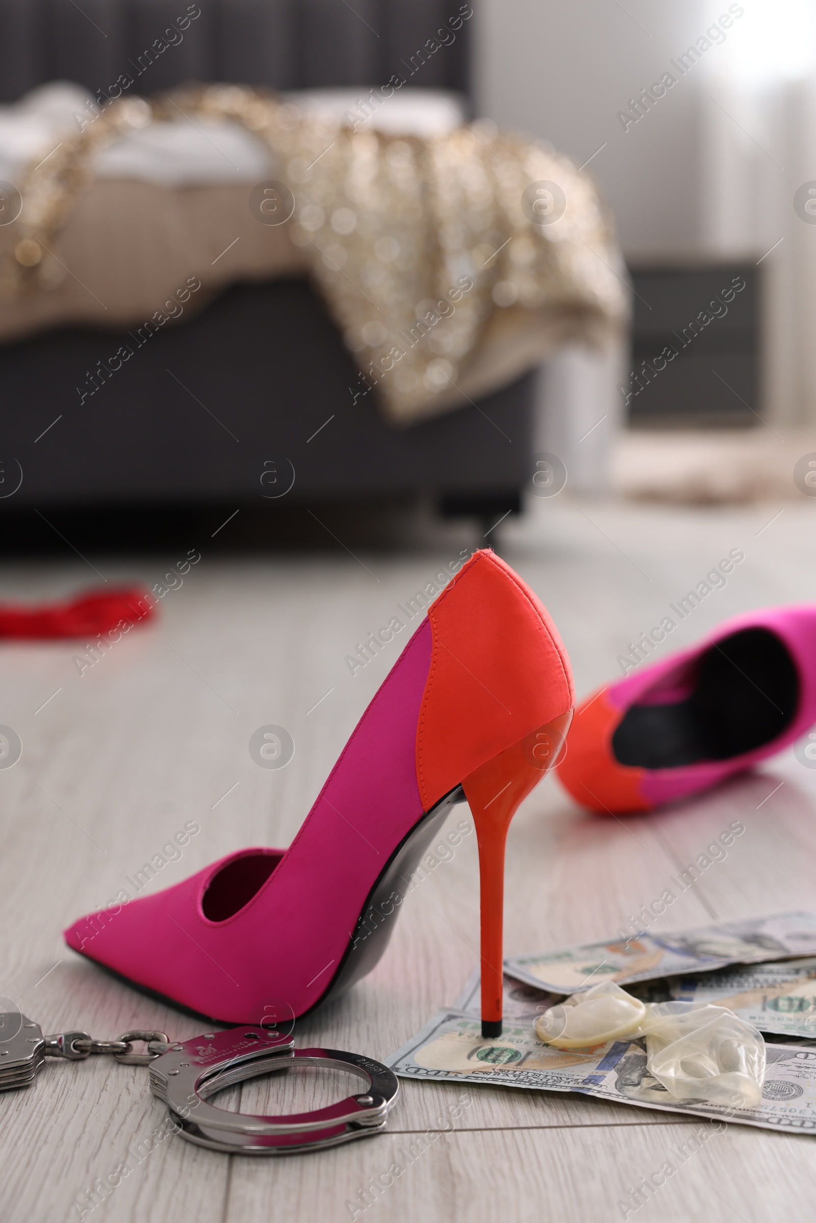 Photo of Prostitution concept. High heeled shoes, dollar banknotes, condoms and handcuffs on floor indoors, space for text.