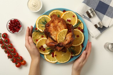 Photo of Woman holding plate with baked chicken and orange slices at white table, top view
