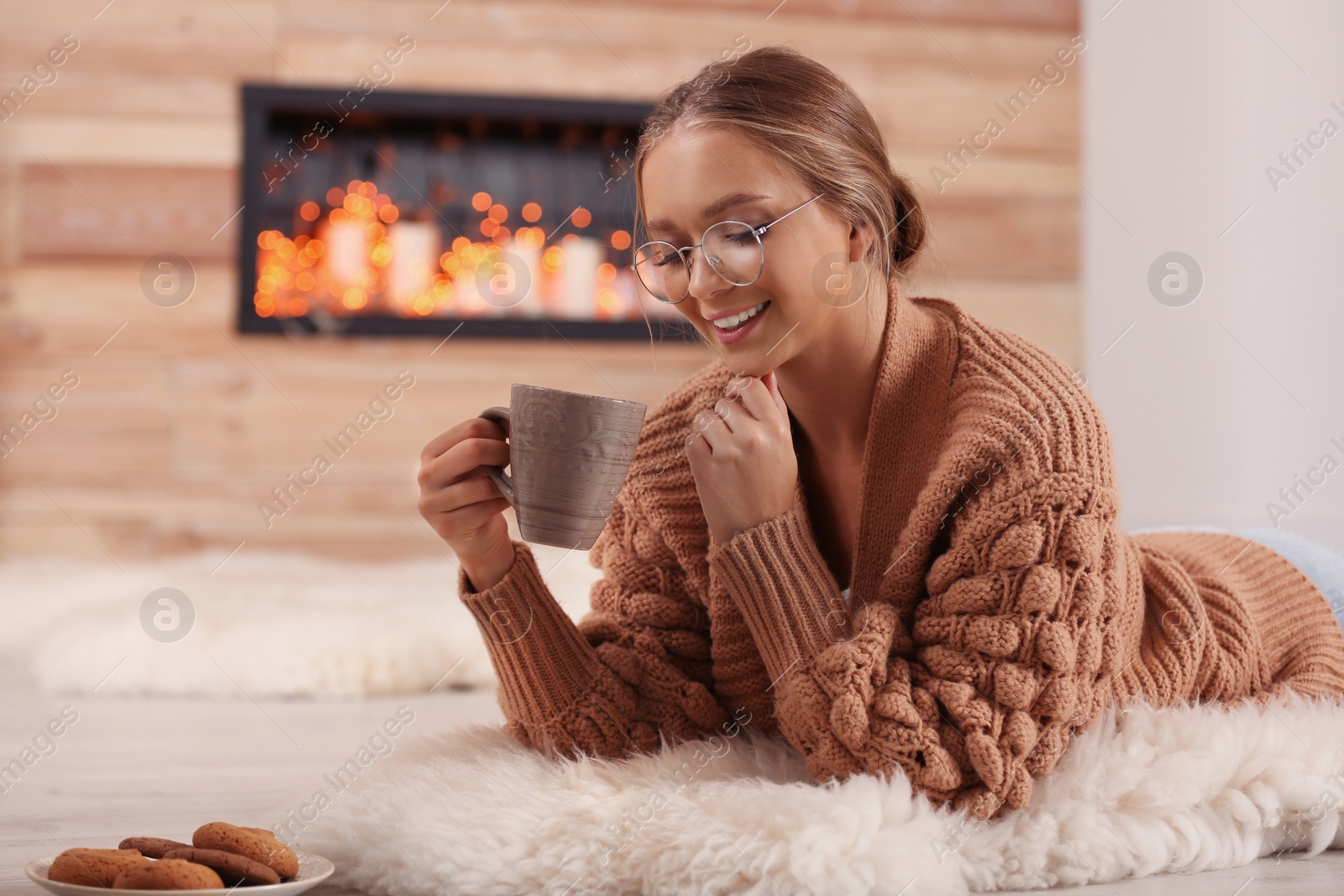 Photo of Beautiful young woman with cup of hot drink on rug at home. Winter atmosphere