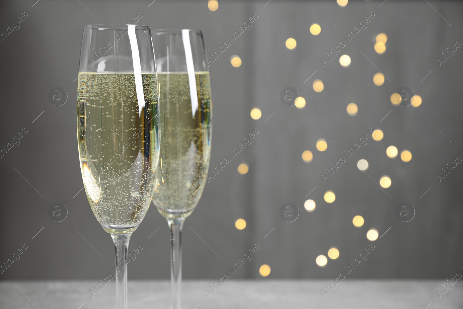 Photo of Glasses of champagne on light grey background with blurred lights. Space for text