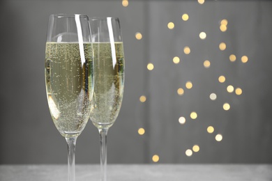 Photo of Glasses of champagne on light grey background with blurred lights. Space for text