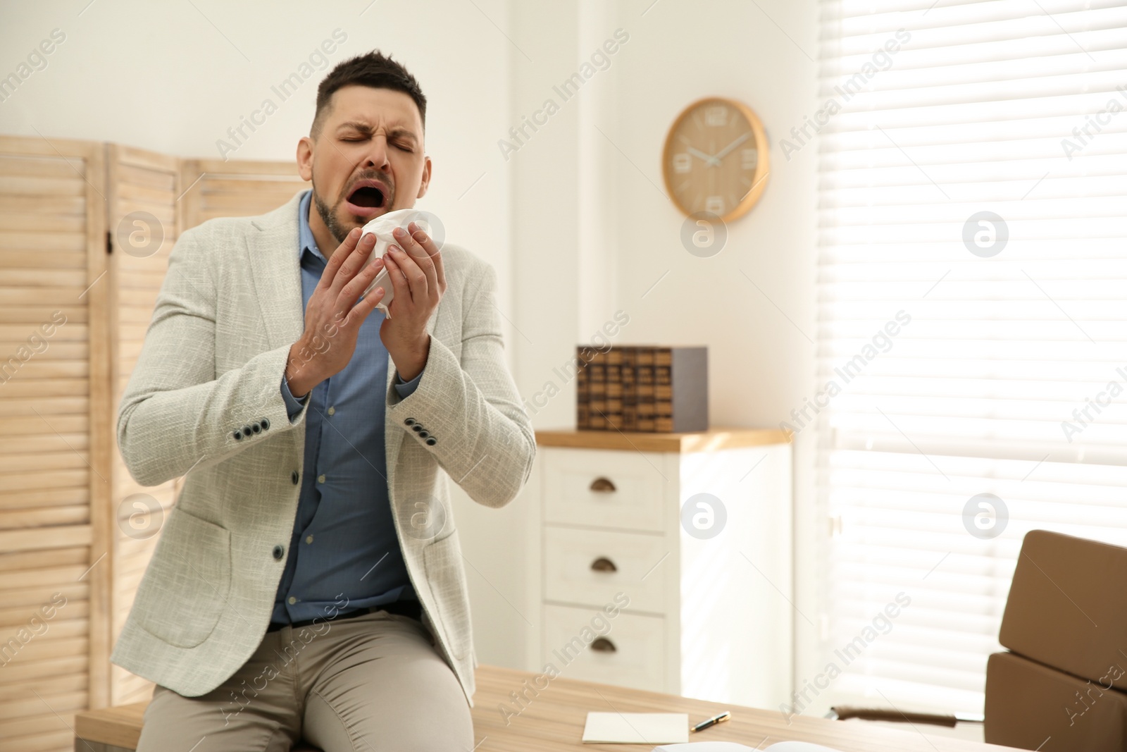 Photo of Sick man sneezing in office. Influenza virus