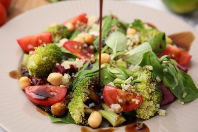 Photo of Pouring balsamic vinegar onto tasty salad in plate, closeup