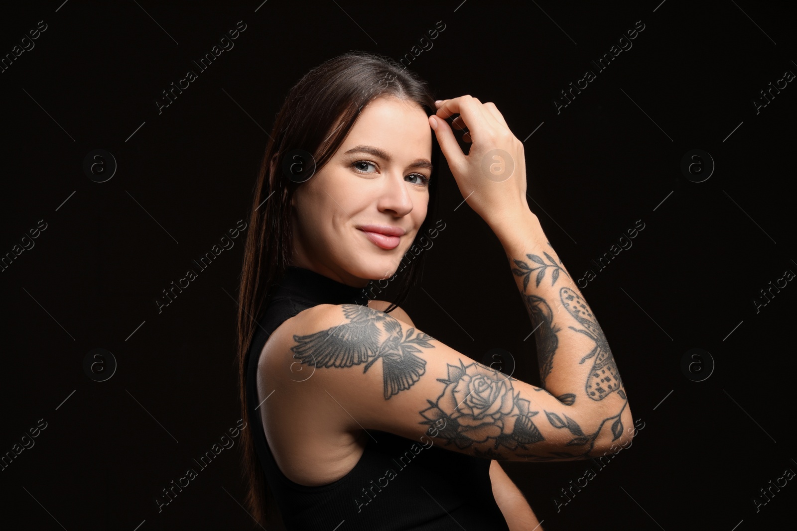 Photo of Beautiful woman with tattoos on arm against black background