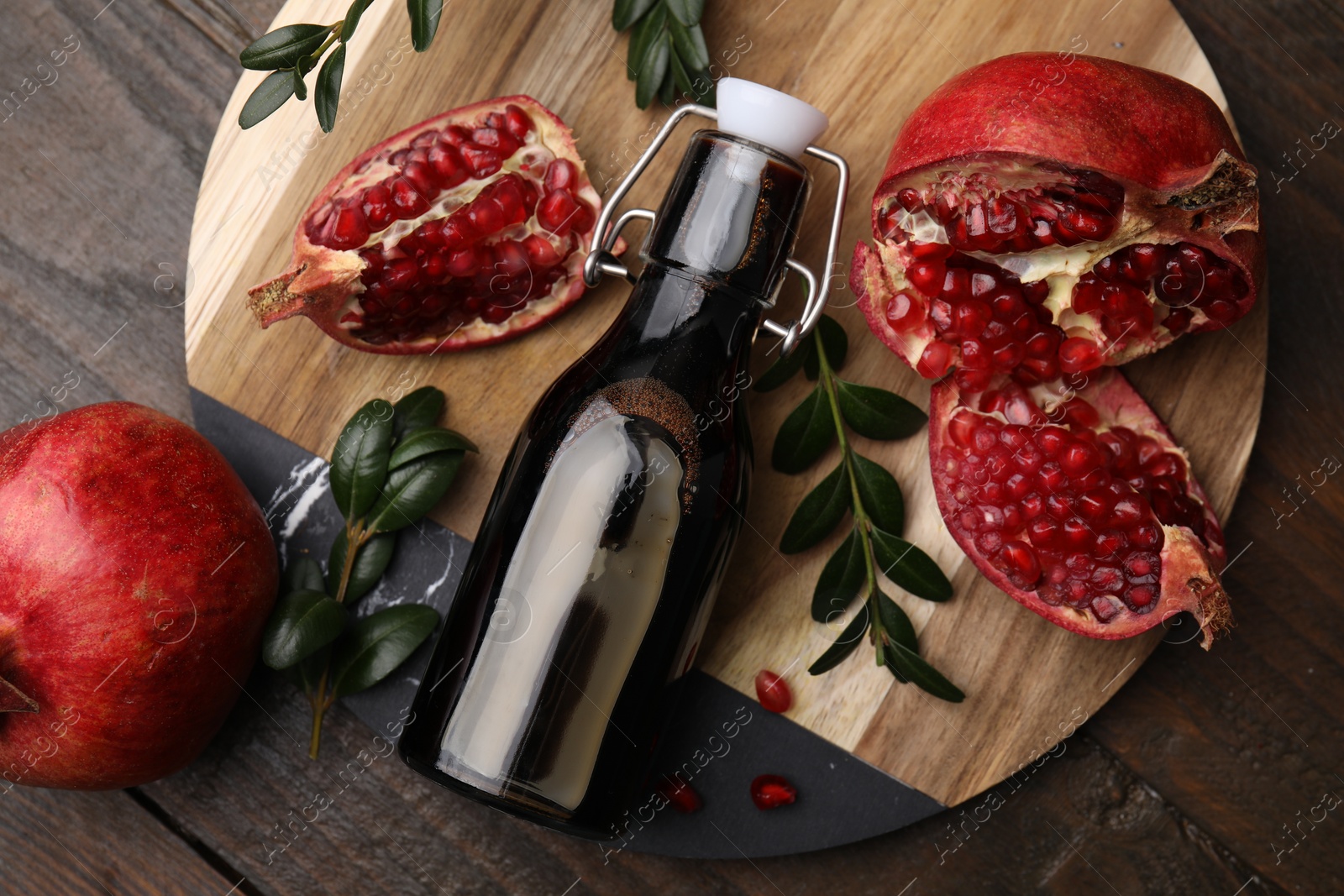 Photo of Tasty pomegranate sauce in bottle, fruits and branches on wooden table, top view