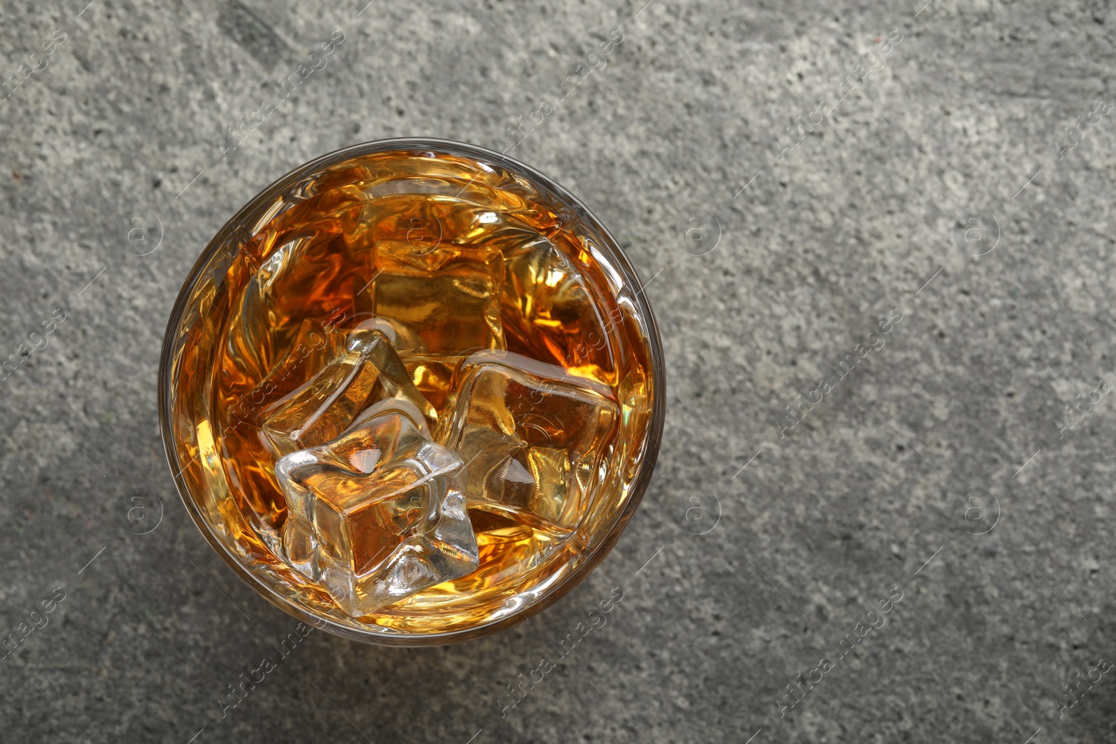 Photo of Whiskey and ice cubes in glass on grey textured table, top view. Space for text