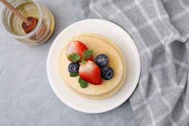 Photo of Stack of tasty pancakes with fresh berries, mint and honey on light grey table, top view