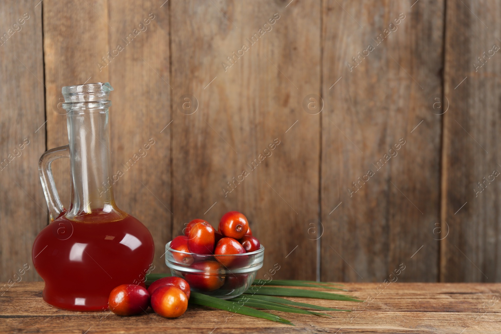 Photo of Palm oil in glass jug, tropical leaf and fruits on wooden table. Space for text