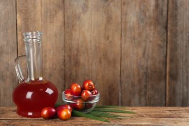 Palm oil in glass jug, tropical leaf and fruits on wooden table. Space for text