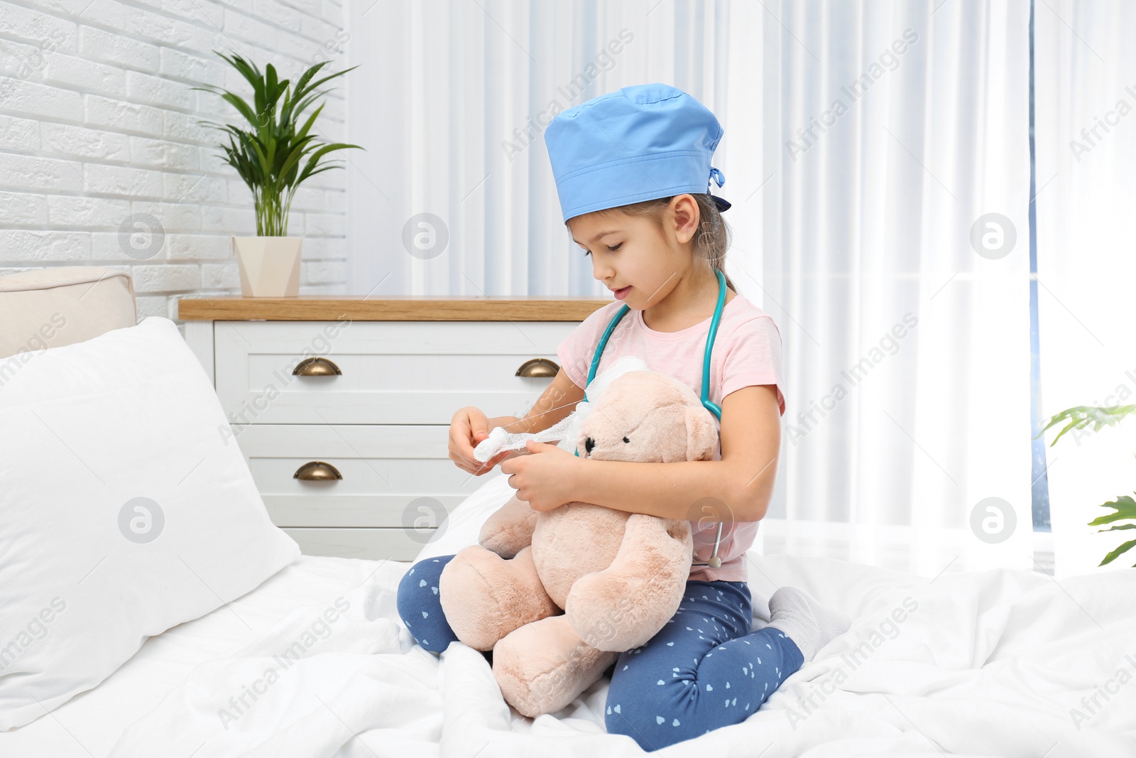 Photo of Cute child playing doctor with stuffed toy on bed in hospital ward