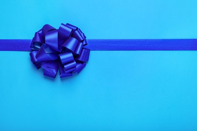 Photo of Ribbon with bow on light blue background, top view. Space for text