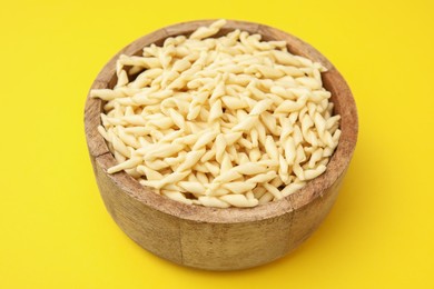 Uncooked trofie pasta in bowl on yellow background, closeup