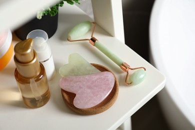 Photo of Gua sha tools, natural face roller and toiletries on white shelf