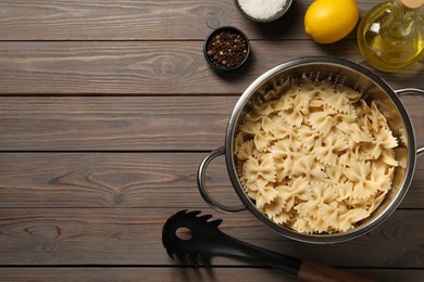 Cooked pasta in metal colander, lemon, oil and spices on wooden table, flat lay. Space for text