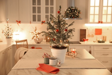 Photo of Small Christmas tree decorated with baubles and festive lights in kitchen