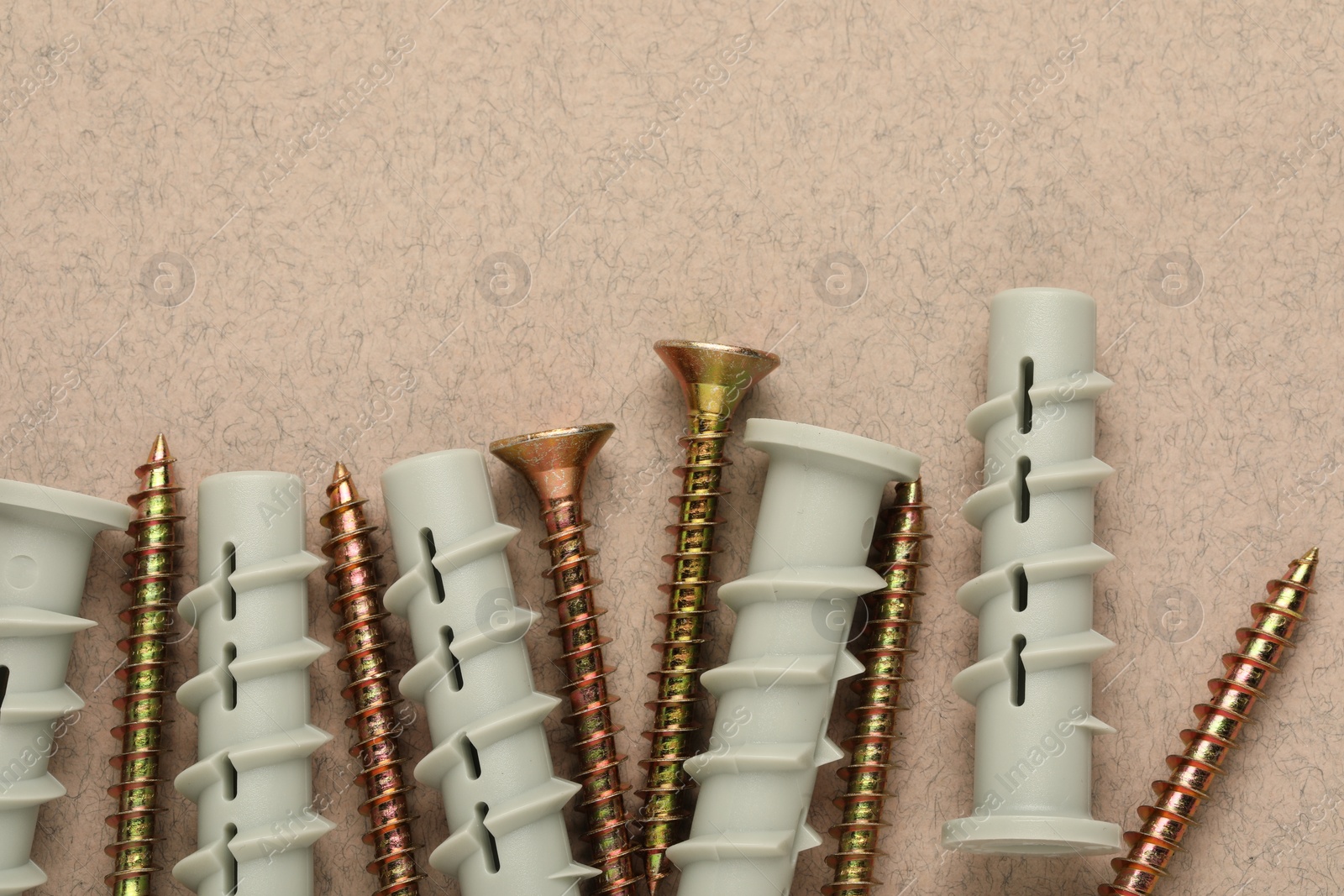 Photo of Many metal screws and white dowels on beige background, flat lay. Space for text