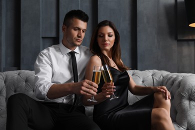 Photo of Beautiful couple with glasses of champagne on sofa indoors. Luxury lifestyle
