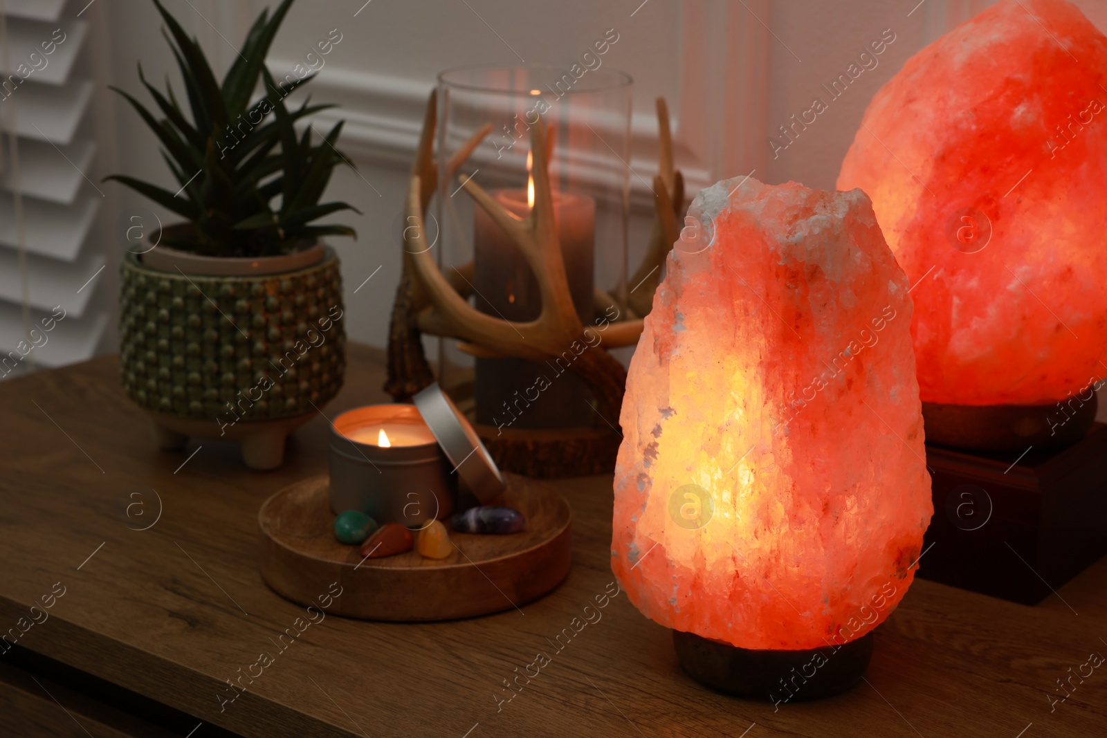 Photo of Himalayan salt lamps, candles, houseplant and gemstones on wooden table near white wall indoors