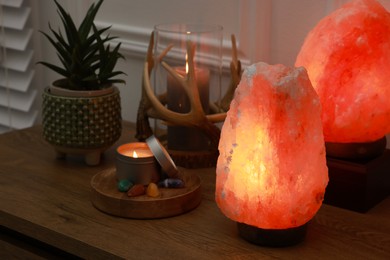 Photo of Himalayan salt lamps, candles, houseplant and gemstones on wooden table near white wall indoors