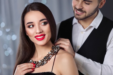 Photo of Man putting jewelry on beautiful young woman against blurred lights