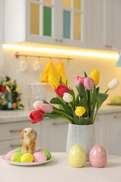 Photo of Bouquet of tulips, painted eggs and Easter decorations on white table in kitchen