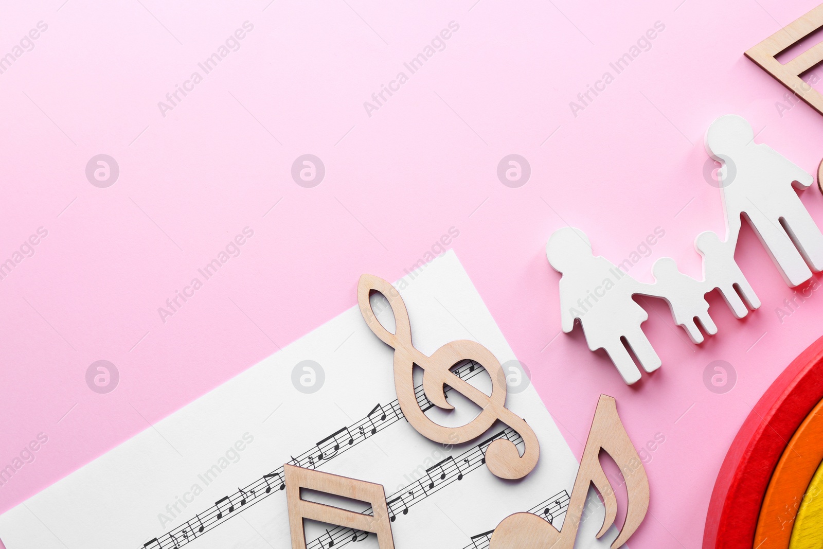 Photo of Baby songs. Music sheet, figures of family, wooden notes and toy rainbow on pink background, flat lay with space for text