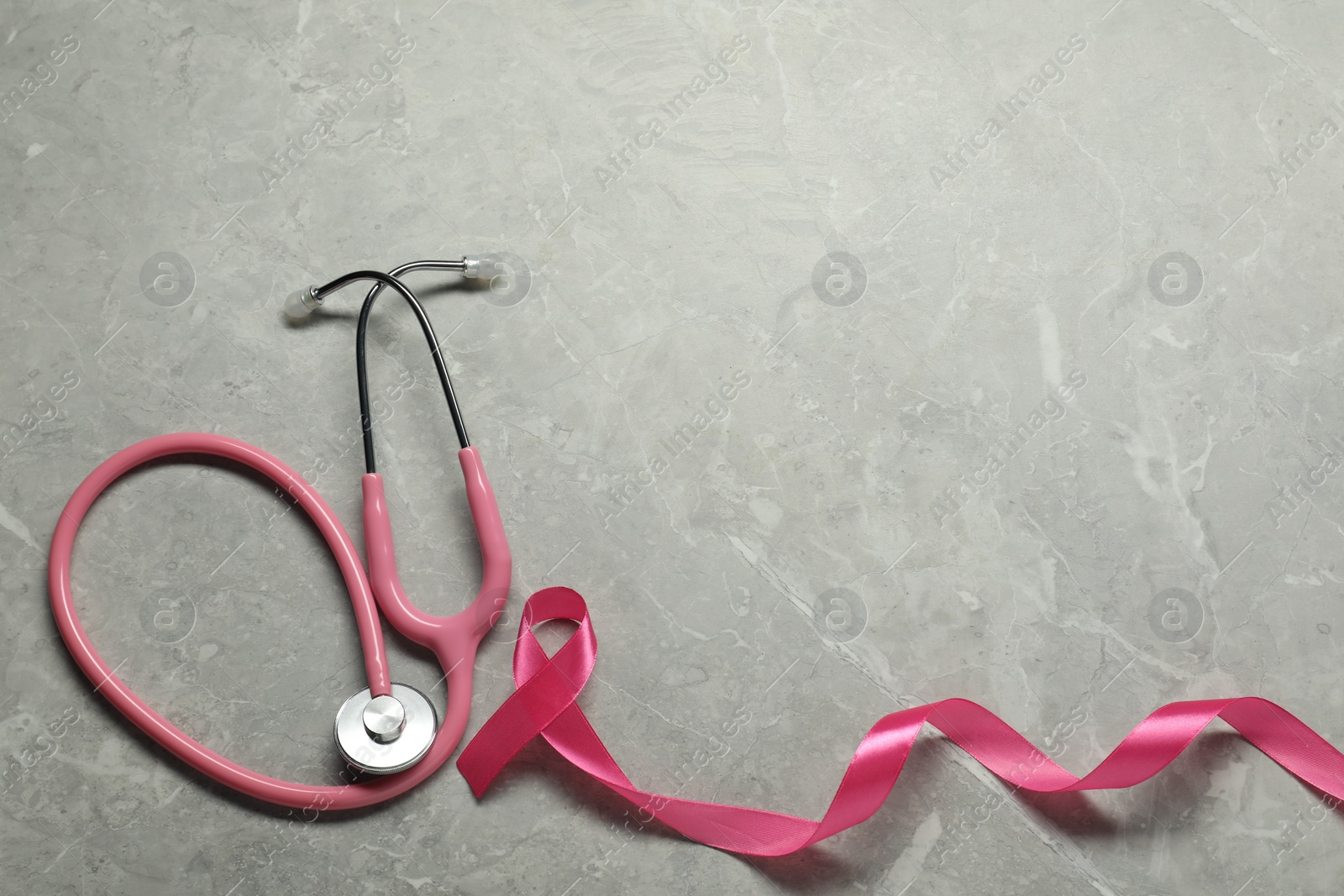 Photo of Breast cancer awareness. Pink ribbon and stethoscope on grey marble table, flat lay. Space for text