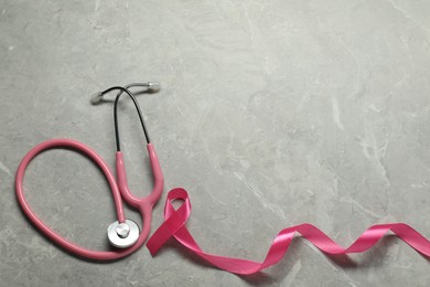 Photo of Breast cancer awareness. Pink ribbon and stethoscope on grey marble table, flat lay. Space for text