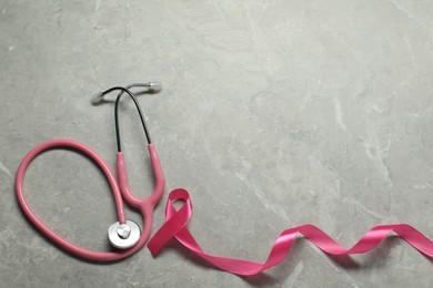 Breast cancer awareness. Pink ribbon and stethoscope on grey marble table, flat lay. Space for text