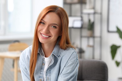 Portrait of beautiful young woman with red hair at home. Attractive lady smiling and looking into camera. Space for text