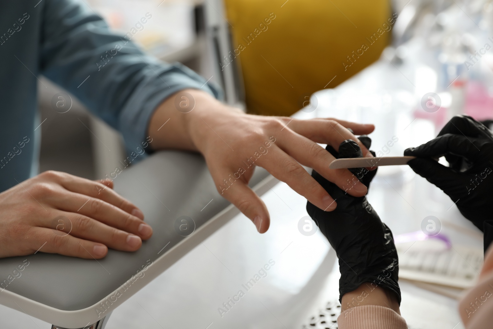 Photo of Professional manicurist filing client's nails in beauty salon, closeup