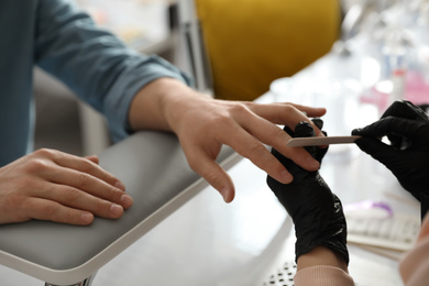 Professional manicurist filing client's nails in beauty salon, closeup