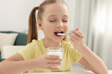 Photo of Cute little girl enjoying tasty yogurt at white table at home
