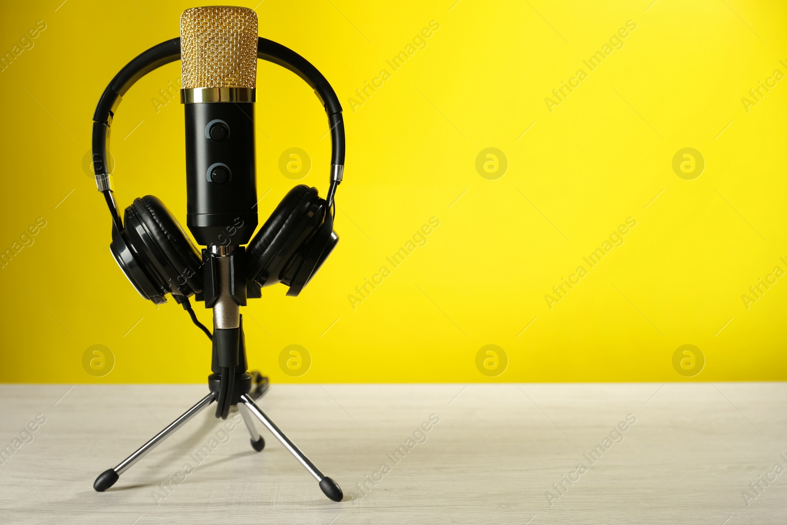 Photo of Microphone and modern headphones on white wooden table against yellow background, space for text