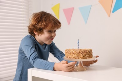 Photo of Cute boy with birthday cake at white table indoors