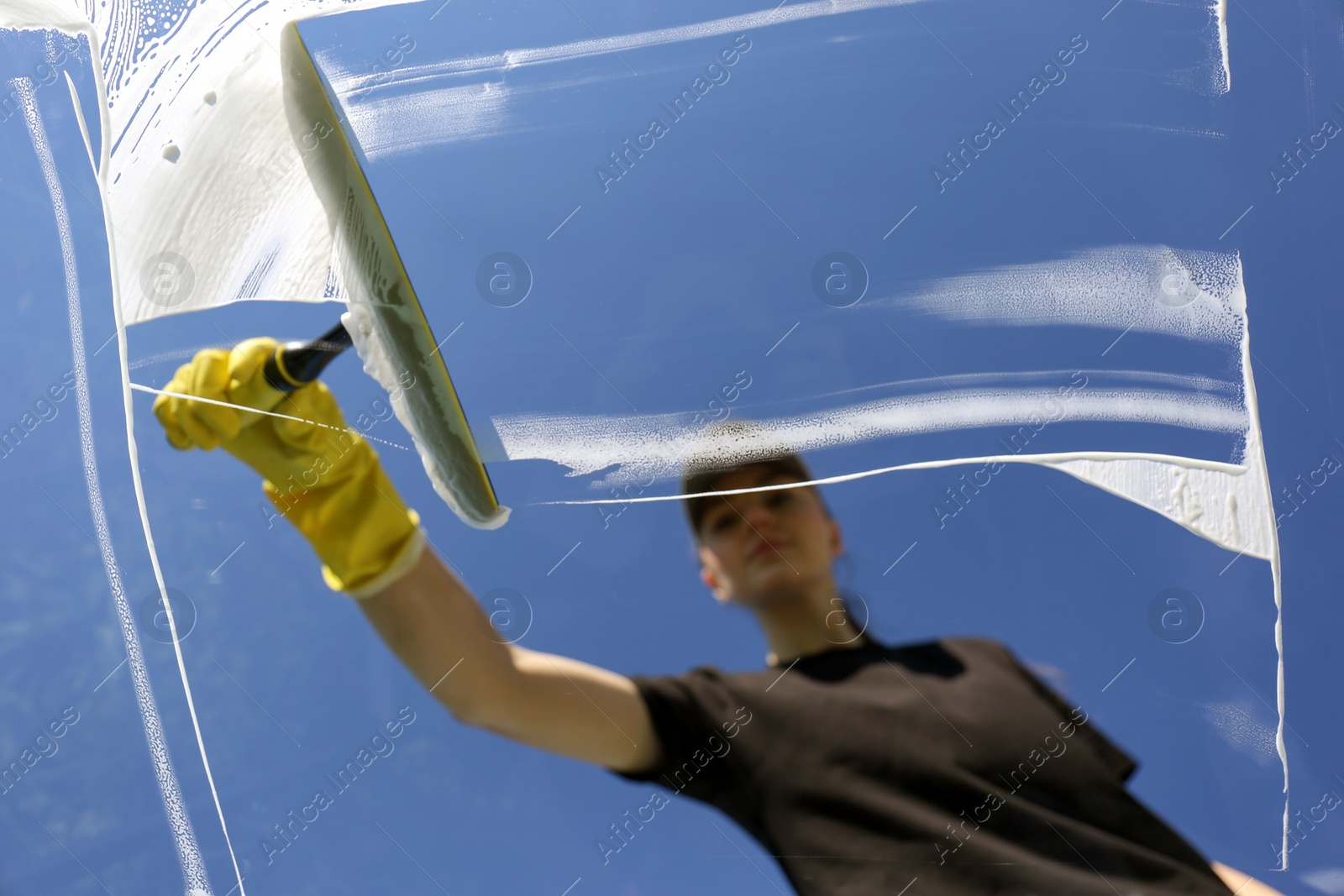 Photo of Woman cleaning glass with squeegee on sunny day