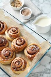 Photo of Tasty cinnamon rolls in baking dish served on white marble table, above view