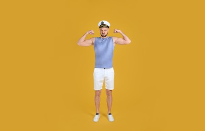 Strong sailor showing biceps on yellow background